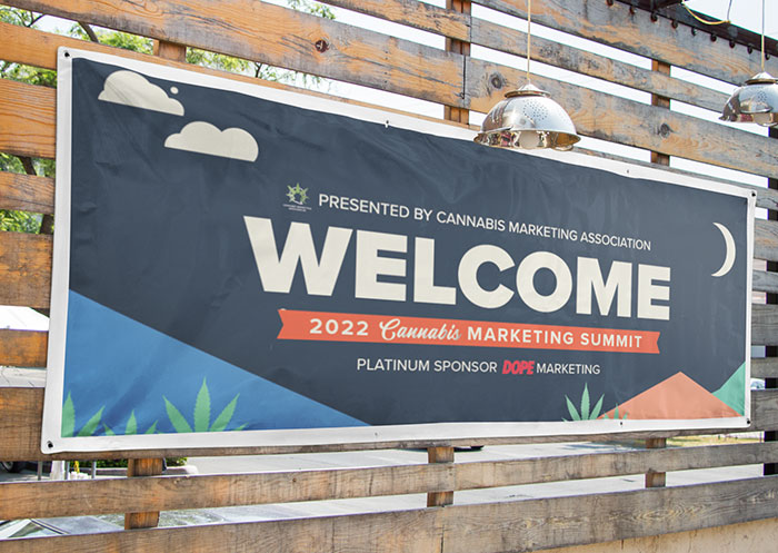 A vinyl sign "Welcome" sign for the 2022 Cannabis Marketing Summit. It is pinned to wooden a fence outside.